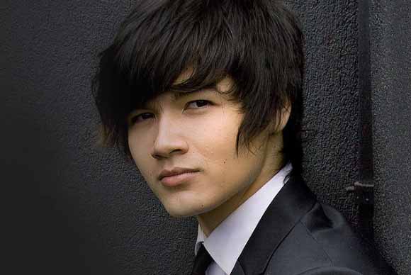 Person in suit leaning against dark wall.
